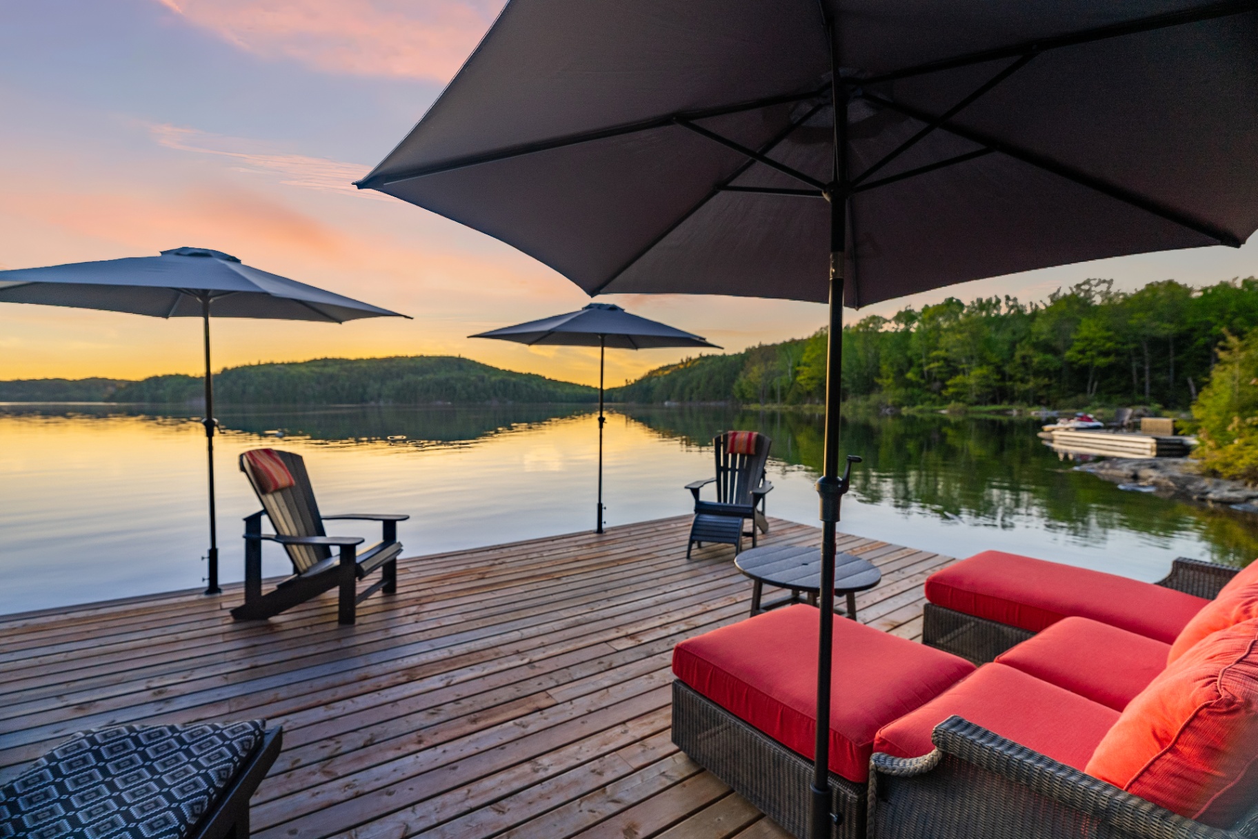 Dock lounge at sunset with red sectional, umbrellas, and Adirondack chairs over still water