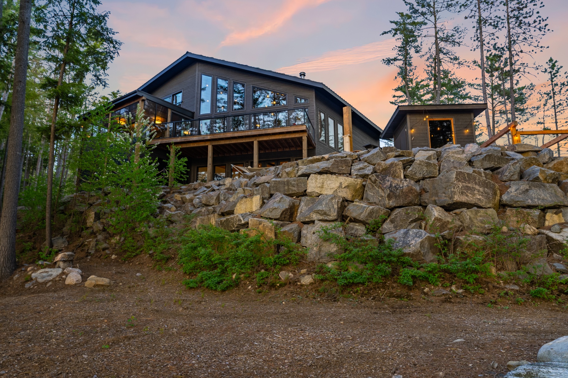 Dramatic rear exterior atop the granite boulder wall glowing at dusk