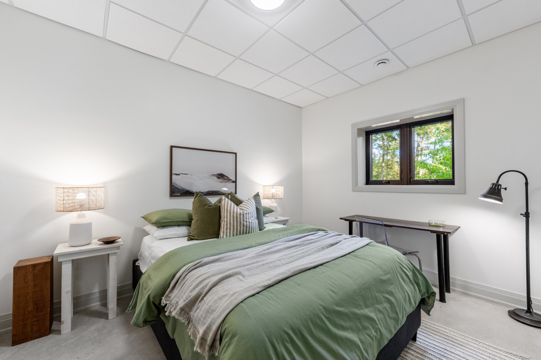 Guest bedroom with green bedding, desk, and forest-view window