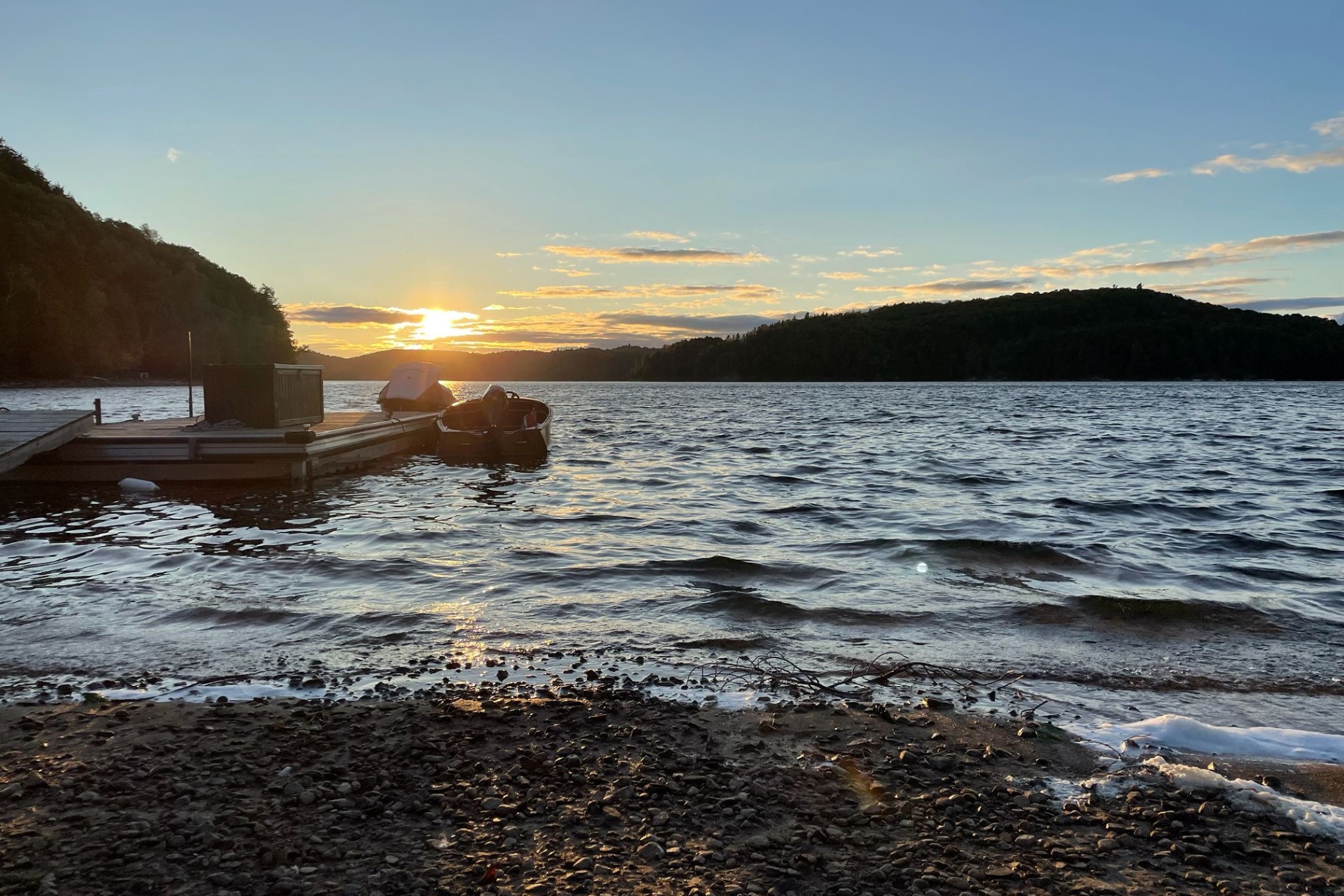 Dock and rowboat at sunset with rippled water and forested hills beyond