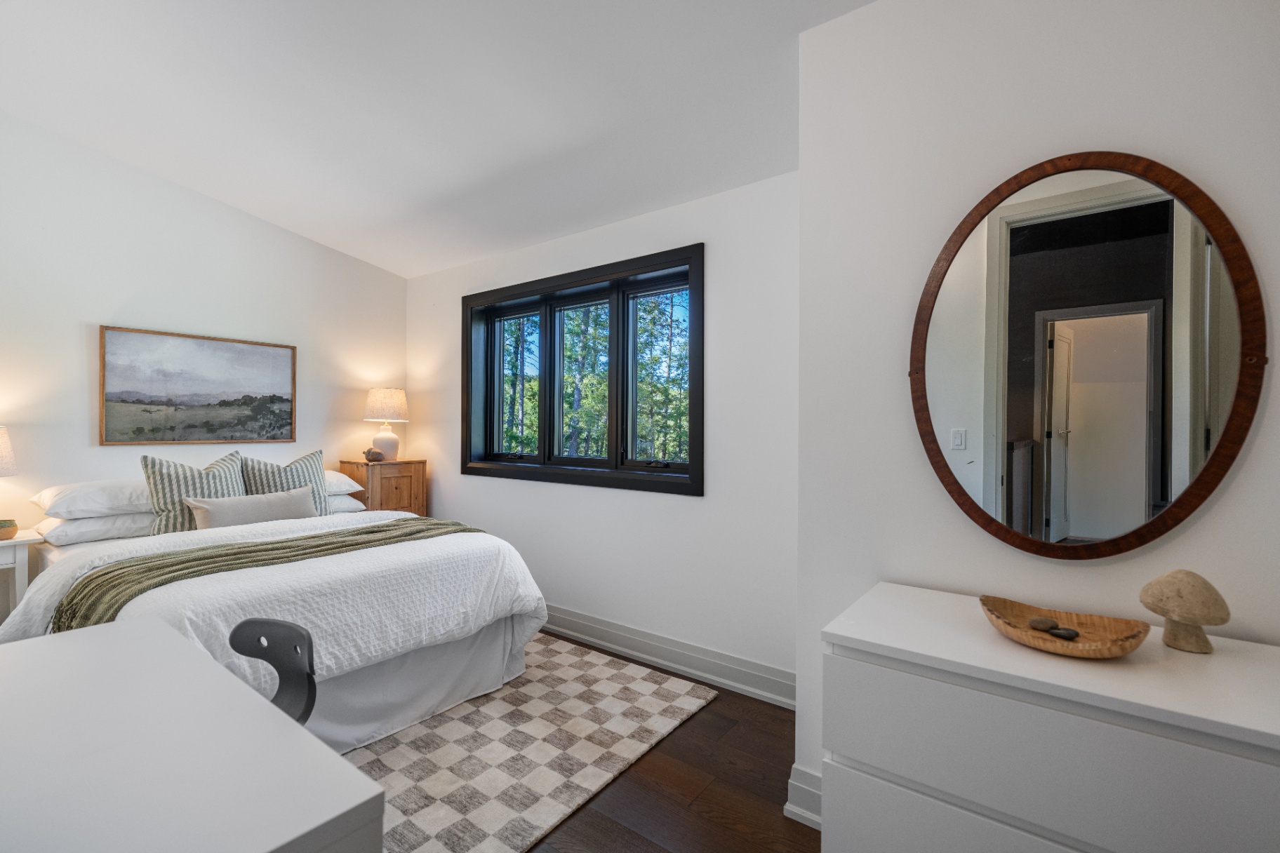 Guest bedroom with round mirror and forest view
