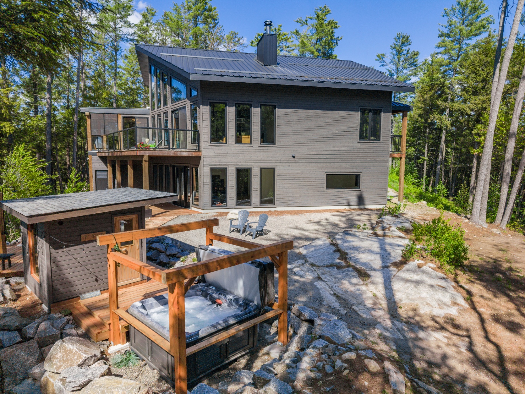 Rear terrace with hot tub, sauna structure, and broad rock apron