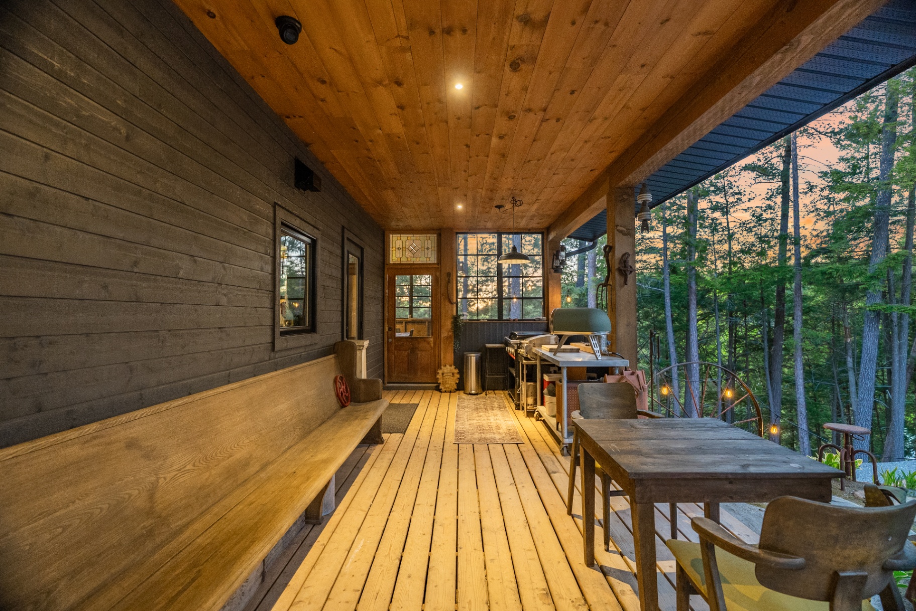 Long view down the covered porch with bench seating, prep area, and forest outlook