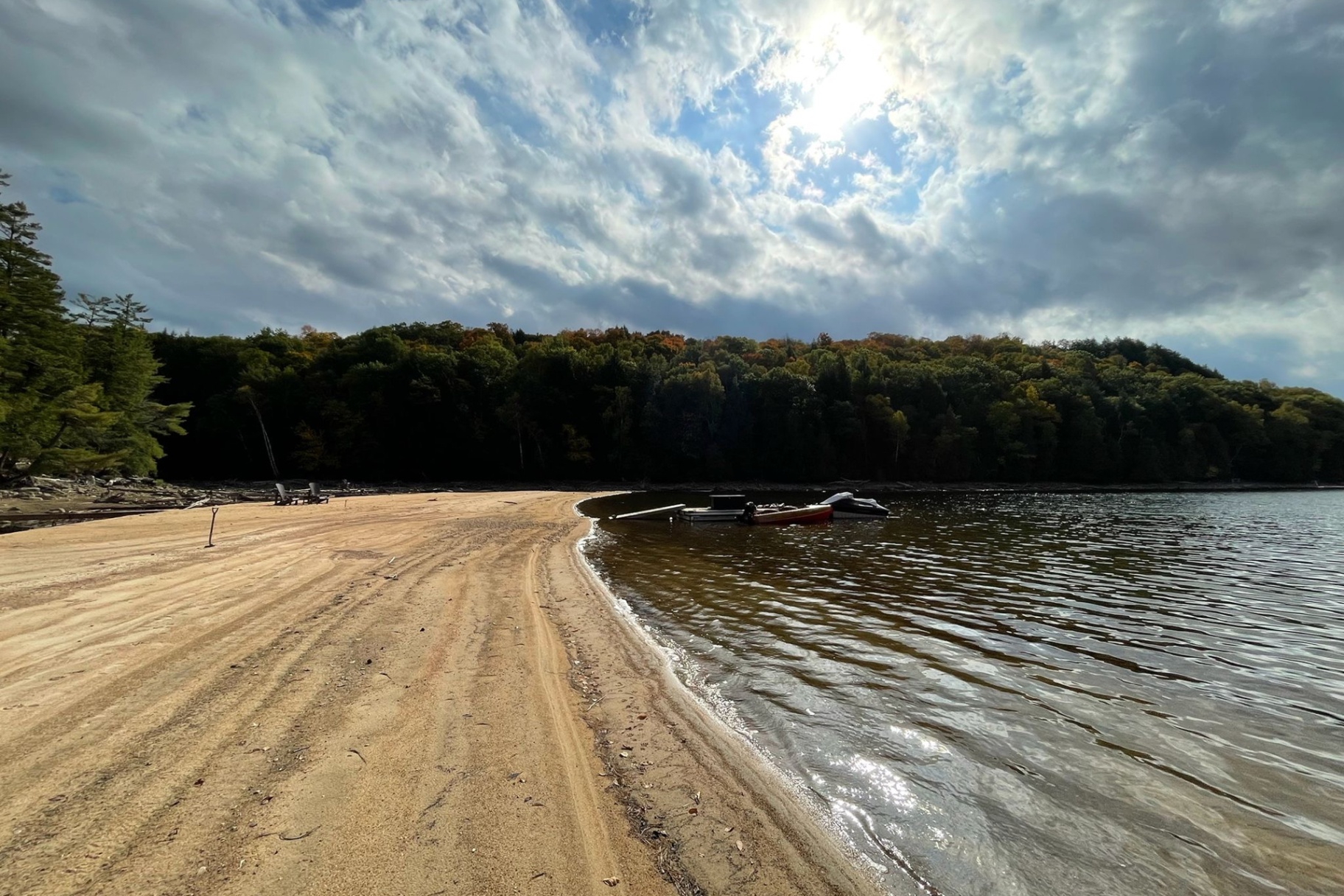 Wide sandy beach curving toward moored boats under dramatic autumn clouds