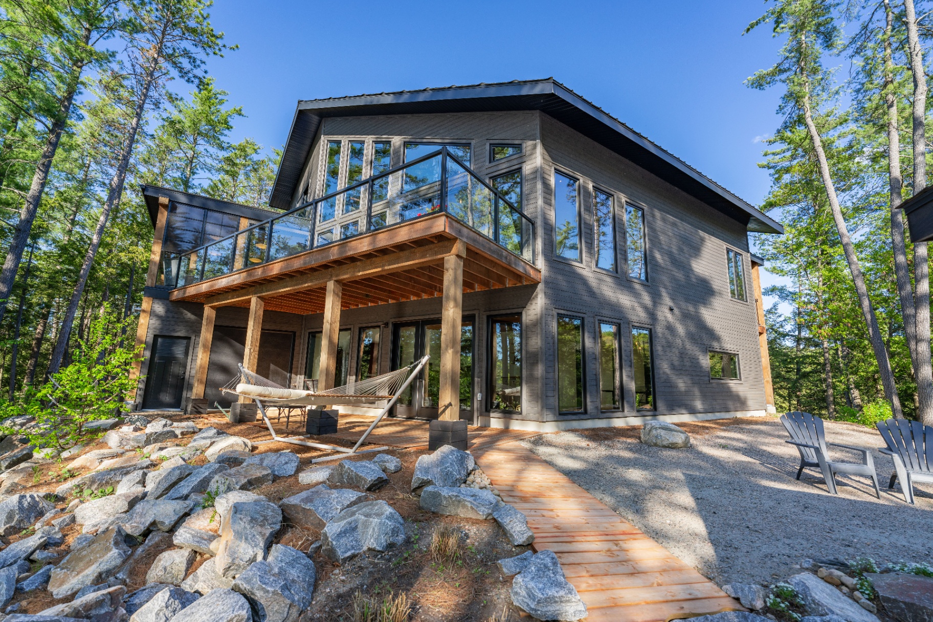 Rear exterior of the lake house with wraparound deck, hammock, and granite landscape
