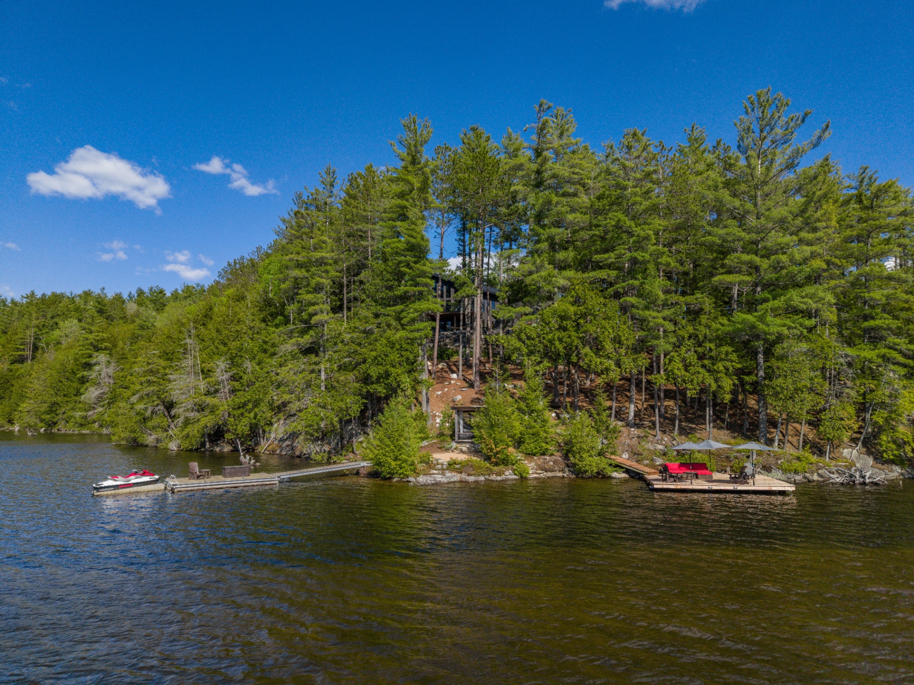 Water-level view of the home tucked into pines above twin docks and lakeside lounge