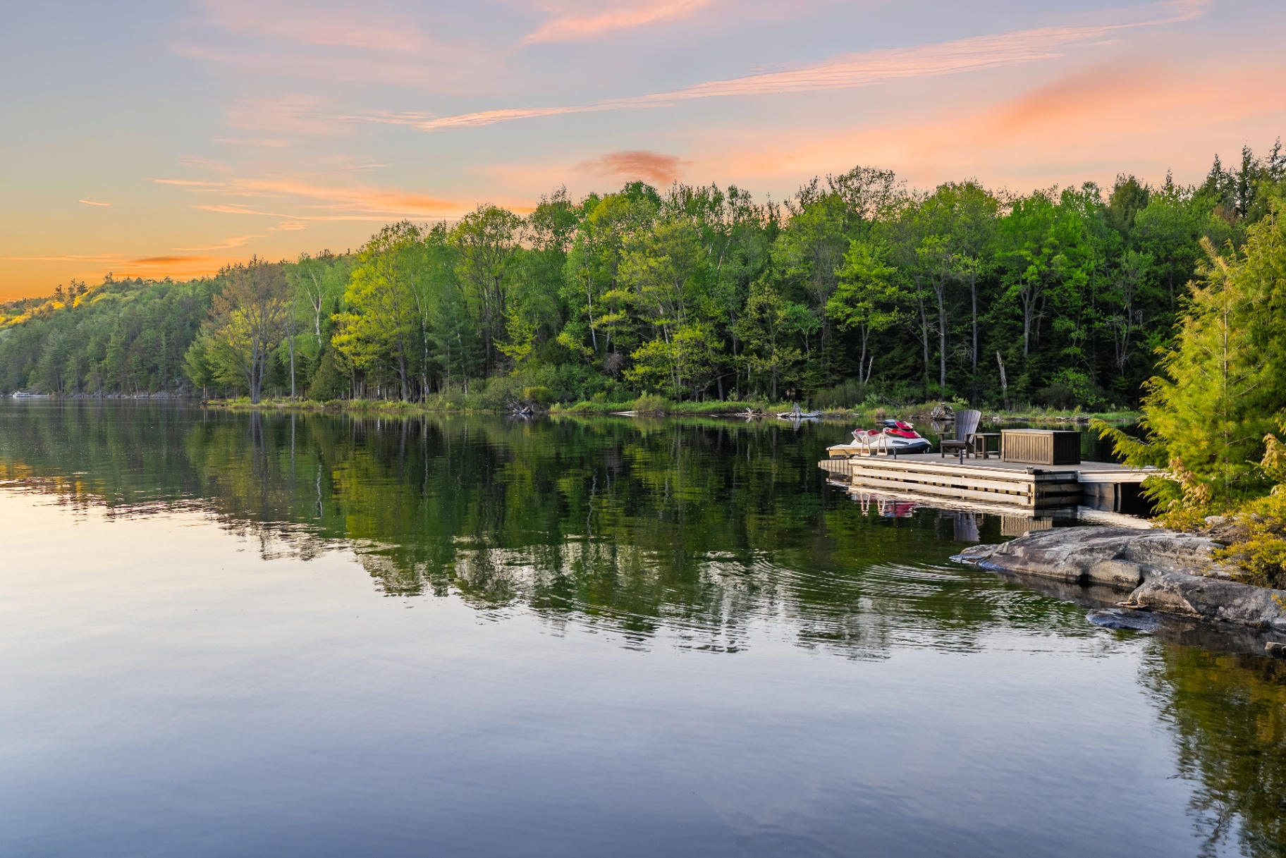 Distant view of the private dock and jet skis tucked into the forested shoreline at dusk