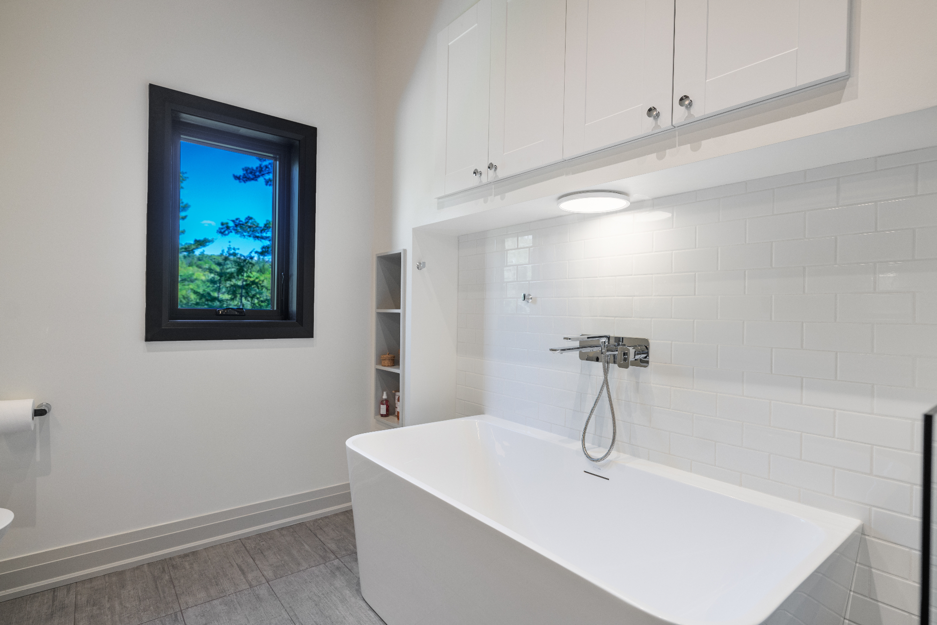 Close view of the soaking tub beneath built-in storage and forest window