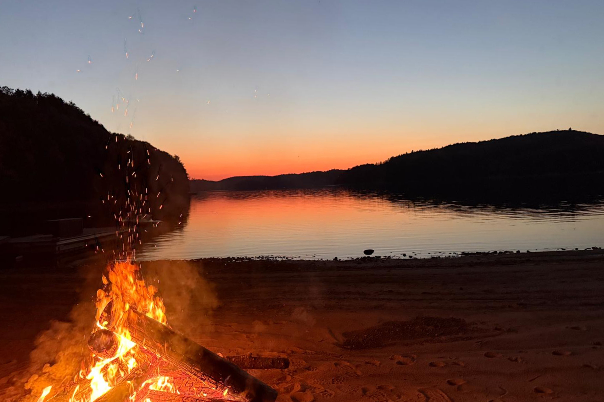 Beach bonfire crackling against a pastel sunset over Redstone Lake
