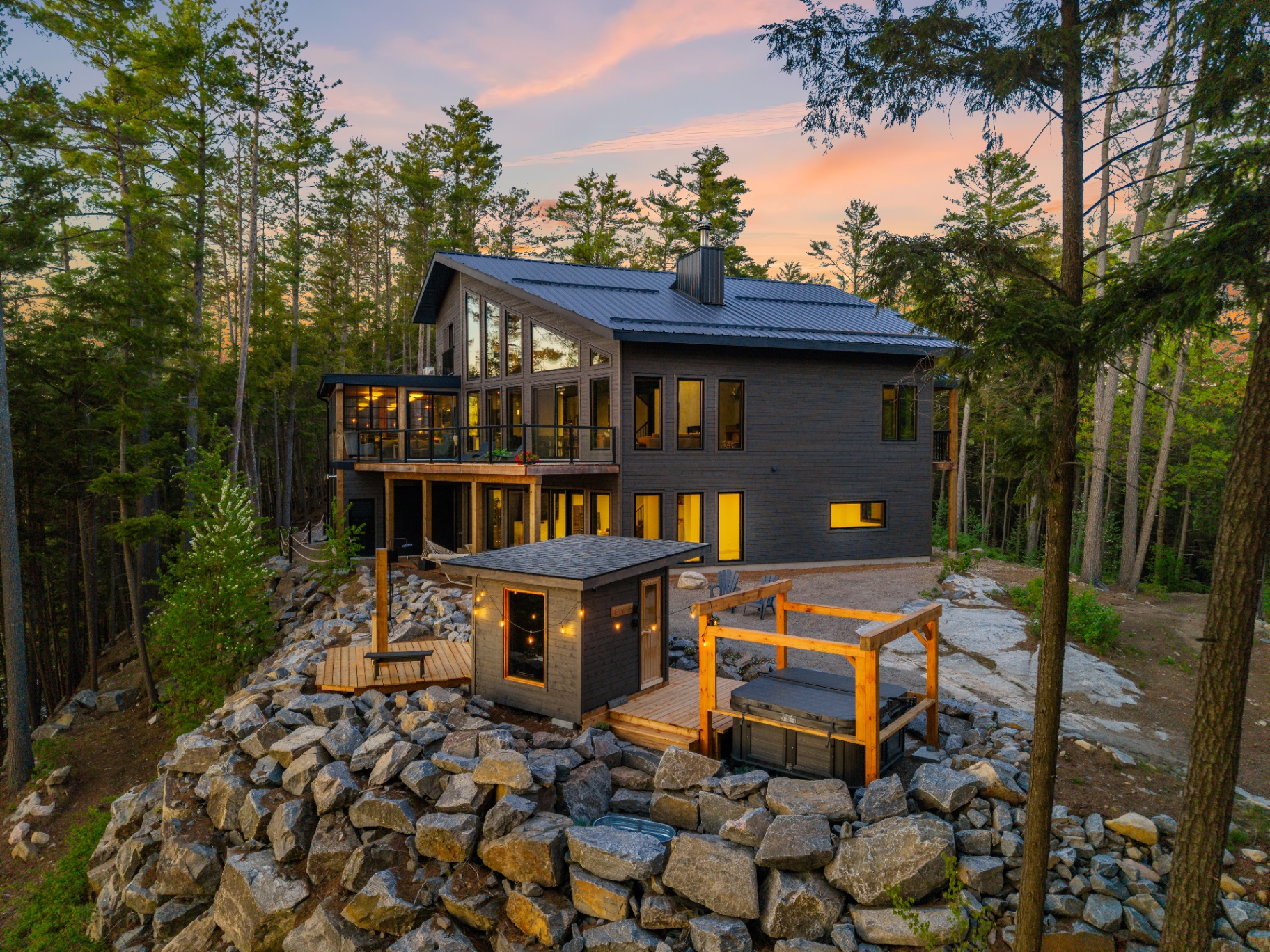 Twilight aerial of the rear exterior with sauna, hot tub, and granite boulder wall