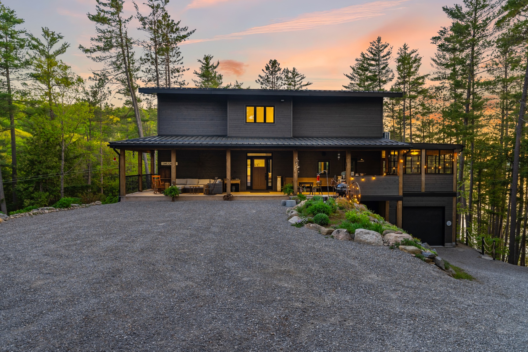 Centered dusk exterior of the lake house with wraparound porch and screened room illuminated