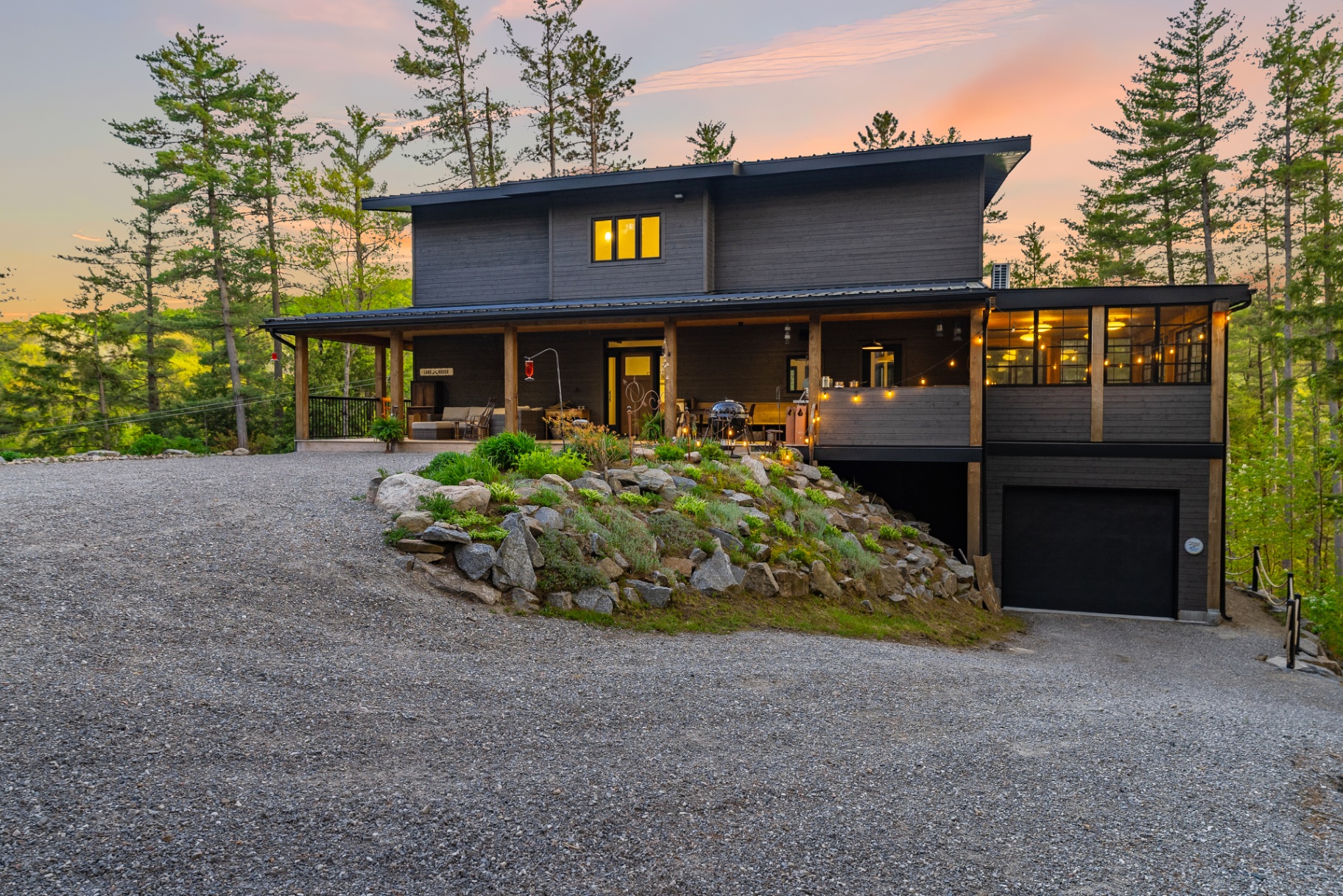 Twilight front exterior with covered porch, landscaped granite, and warm interior glow