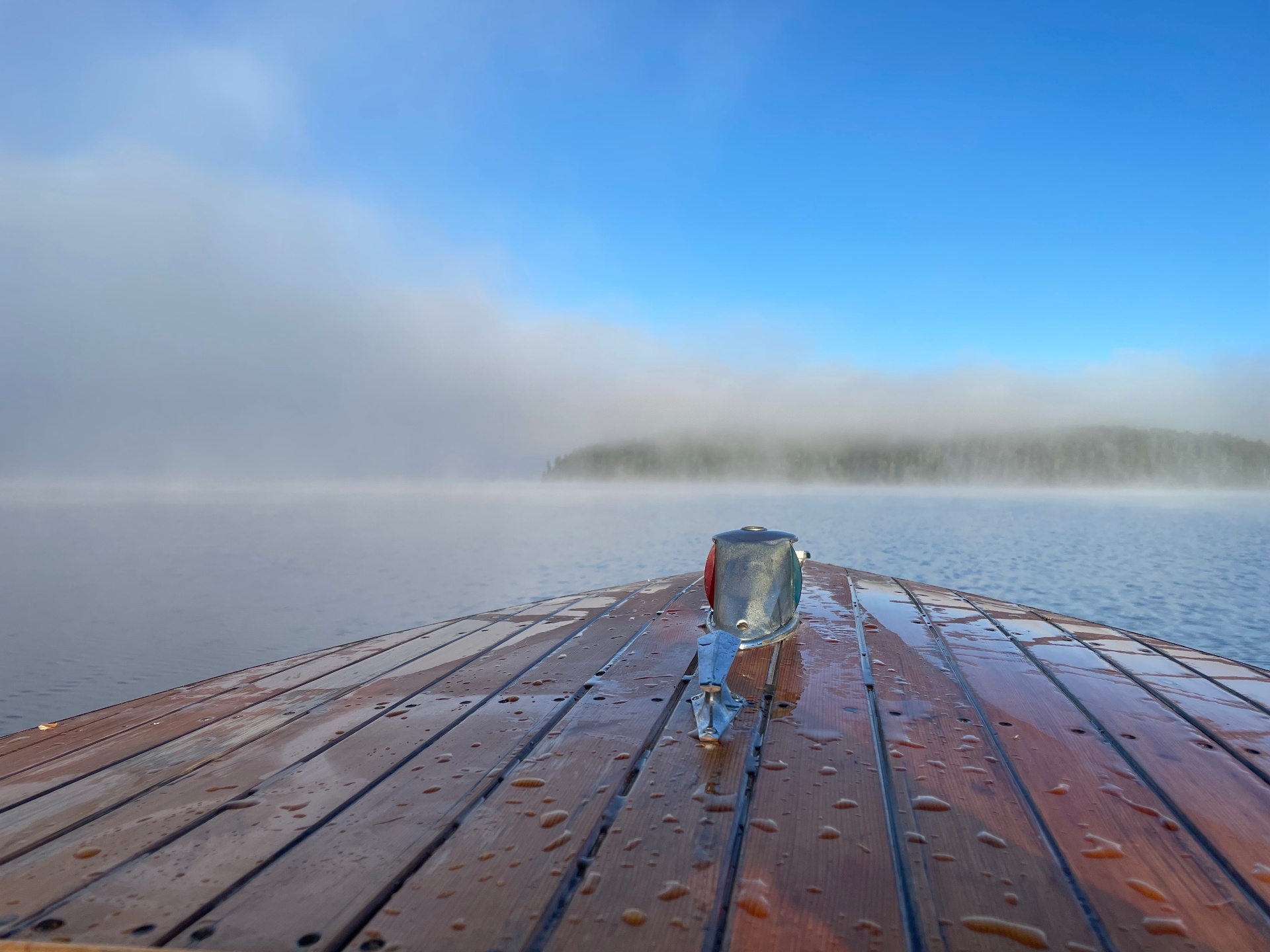 Bow of a classic wooden boat gliding across a misty Redstone Lake morning