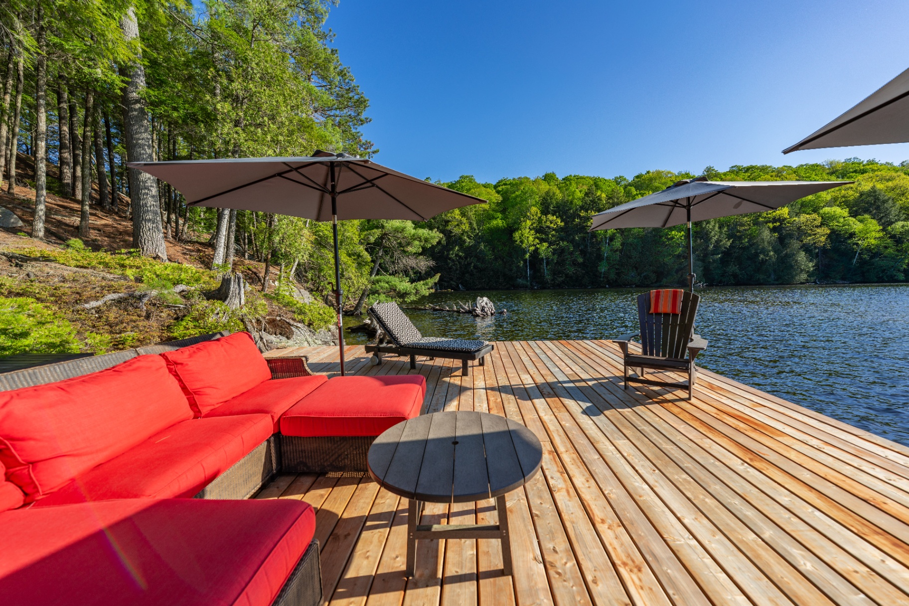 Red sectional and umbrellas on cedar dock with pines and lake beyond
