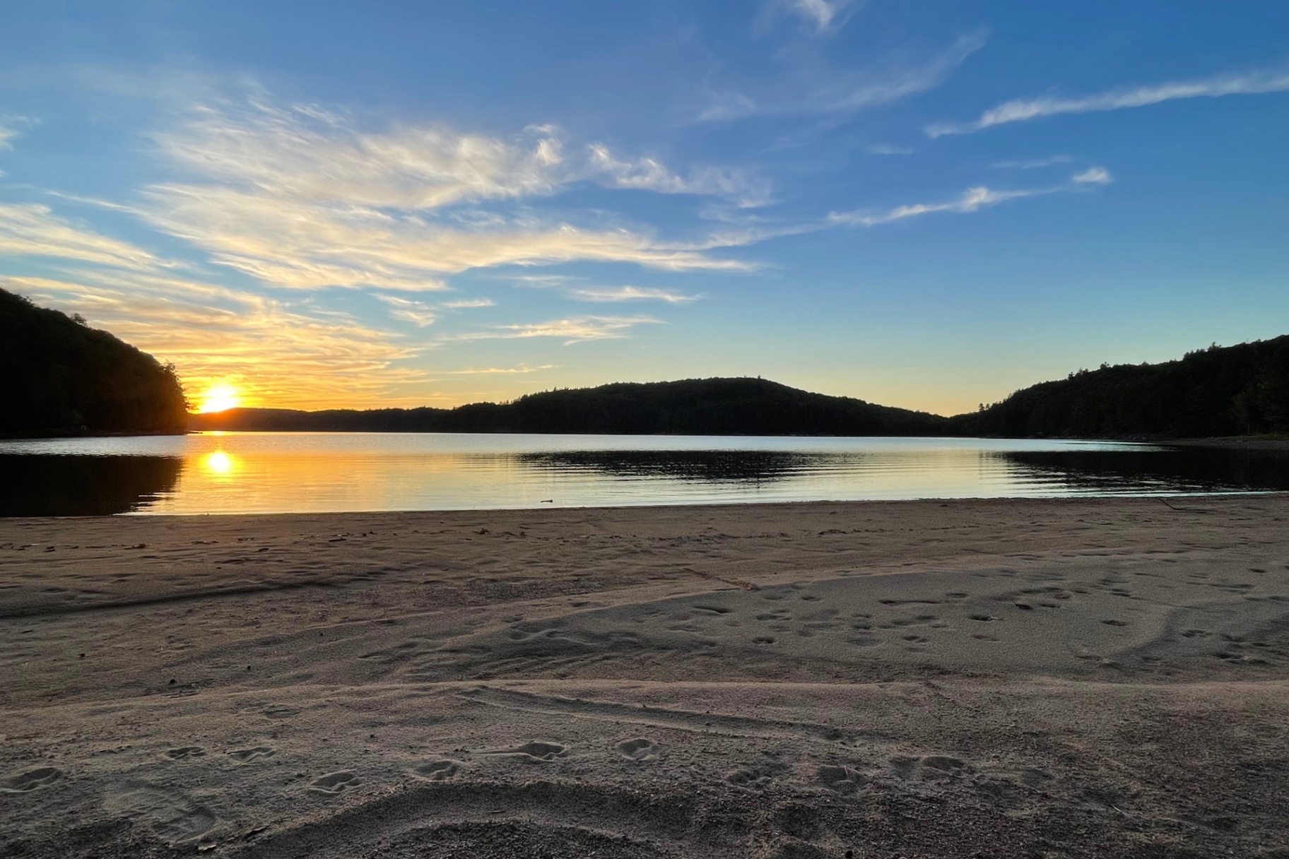 Wide sandy beach and calm lake mirroring a soft sunset sky