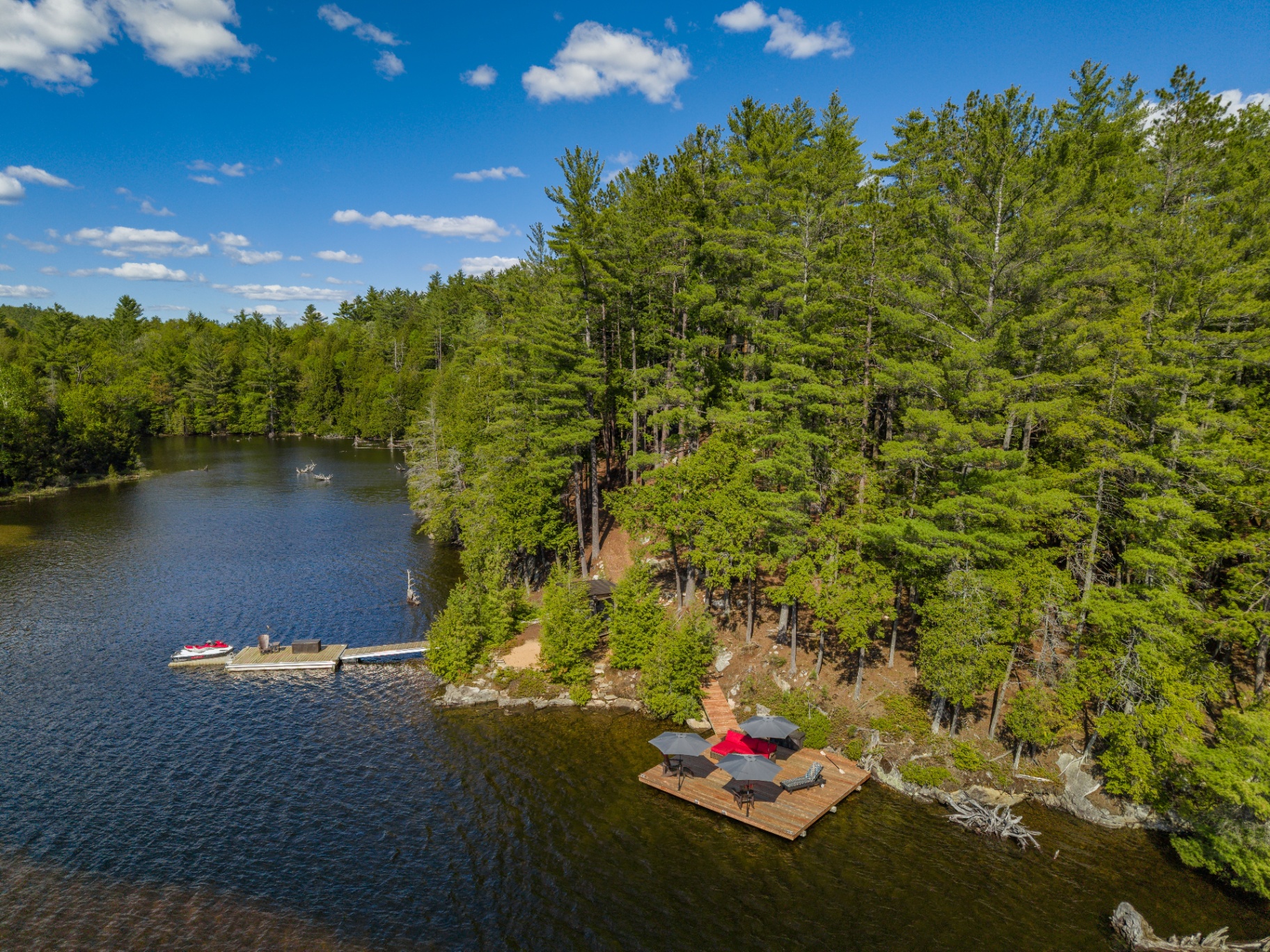 Aerial shoreline view with floating lounge dock, jet ski dock, and wooded point