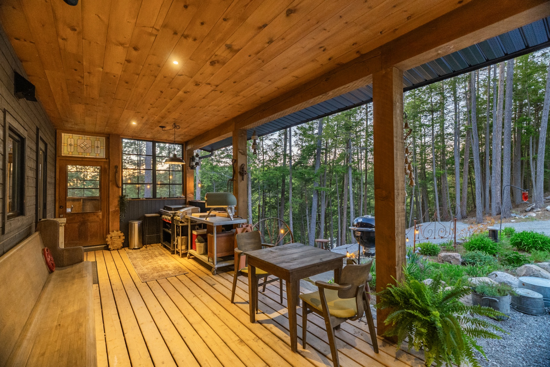 Covered porch dining and grill area with warm timber ceiling at dusk
