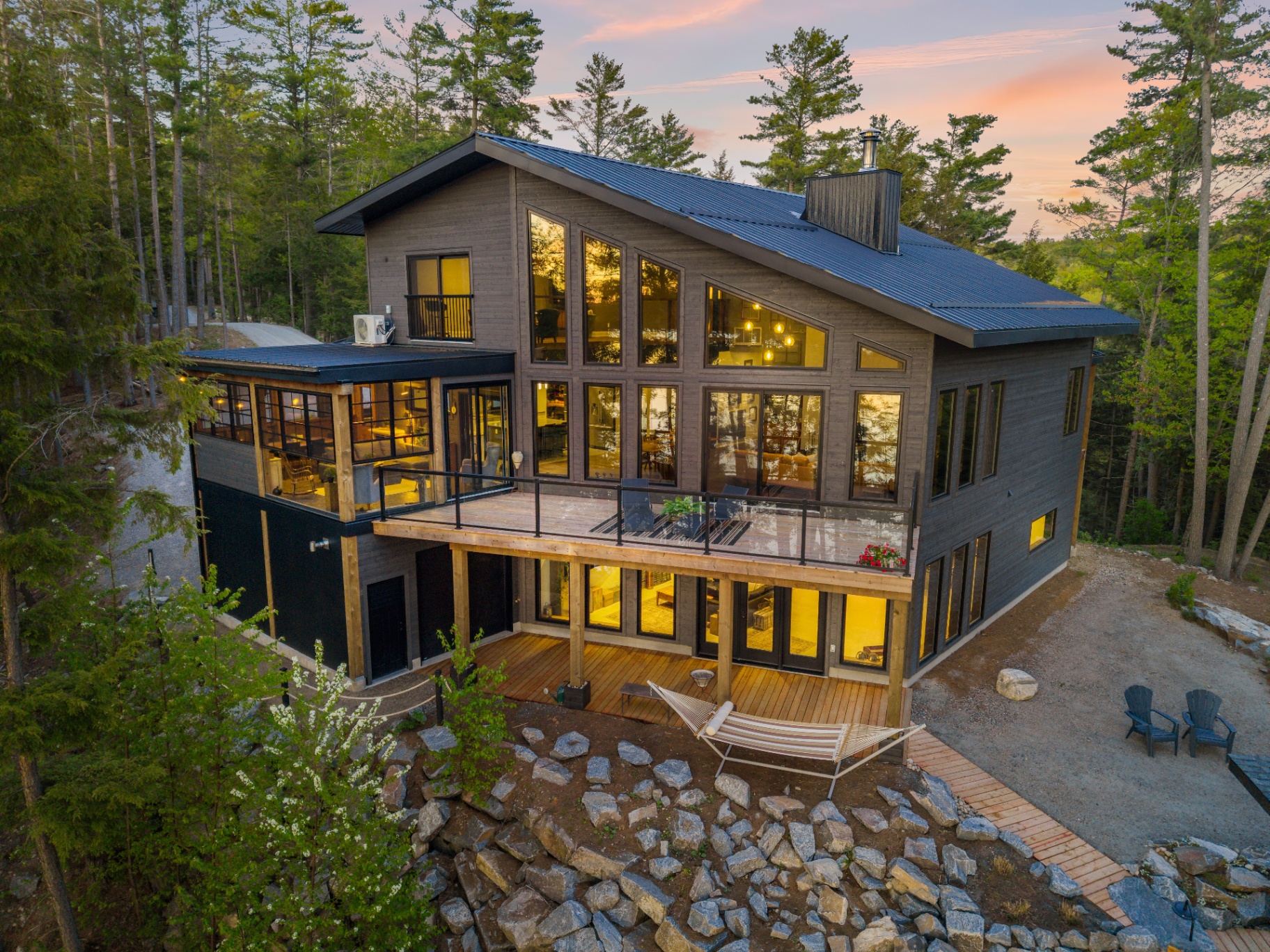 Dusk drone view of the lake-facing rear elevation with deck, screened room, and hammock